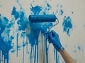 On a white surface, a hand with a blue paint roller drips paint Royalty Free Stock Photo