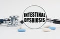 On a white surface lie pills, a stethoscope and a magnifying glass with the inscription - INTESTINAL DYSBIOSIS