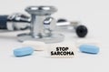 On a white surface lie pills, a stethoscope and a tablet with the inscription - STOP SARCOMA