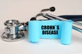 On a white surface lies a stethoscope and a blue roll of paper with the inscription - CROHNS DISEASE