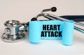 On a white surface lies a stethoscope and a blue roll of paper with the inscription - HEART ATTACK