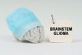 On a white surface next to the brain there is a notepad with the inscription - Brainstem glioma