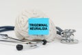 On a white surface next to the stethoscope lies a brain on which a sticker with the inscription - Trigeminal neuralgia Royalty Free Stock Photo