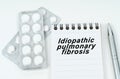 On a white surface are pills in a package, a pen and a notepad with the inscription - Idiopathic pulmonary fibrosis