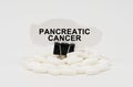 On a white surface are pills and torn paper with the inscription - Pancreatic cancer