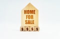 On a white surface stands a wooden model of a house with the inscription - Home For Sale