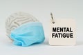 On a white surface there is a brain with a blue mask and a notepad with the inscription - Mental Fatigue