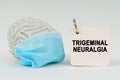 On a white surface there is a brain with a blue mask and a notepad with the inscription - Trigeminal neuralgia Royalty Free Stock Photo