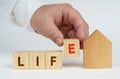 On a white surface there is a model of a house, next to it a man has placed cubes with the inscription - life Royalty Free Stock Photo