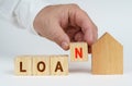 On a white surface there is a model of a house, next to it a man has placed cubes with the inscription - LOAN Royalty Free Stock Photo