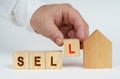 On a white surface there is a model of a house, next to it a man has placed cubes with the inscription - SELL Royalty Free Stock Photo