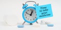 On a white surface, there are tablets and an alarm clock with a sticker that says - Time to take your medicine Royalty Free Stock Photo