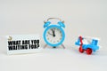 On a white surface there is a toy plane, an alarm clock and a sign with the inscription - What Are You Waiting For Royalty Free Stock Photo