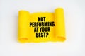 On a white surface, a yellow scroll of paper with the inscription - NOT PERFORMING AT YOUR BEST Royalty Free Stock Photo