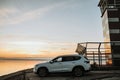 White compact SUV car with sport and modern design parked on concrete road by the sea near the beach at sunset Royalty Free Stock Photo