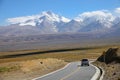 White SUV drives down an empty asphalt road leading to the snowy mountains. Royalty Free Stock Photo