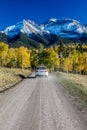 White SUV drivews down Country Road 12 out of Ridgway Colorado towards San Juan Mountains with Autumn Color Royalty Free Stock Photo