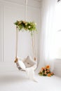 White swing chair with flowers hanging from it's sides and window in the background. Generative AI Royalty Free Stock Photo