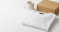 White T Shirt Folded with Coffee Mug and Cardboard Box on White Surface Royalty Free Stock Photo