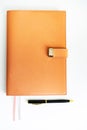 A closed orange notebook lies on a white table, and next to it is a black pen. Royalty Free Stock Photo