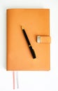 An orange notebook with a magnetic clasp sits on a white table with a black pen on it. Royalty Free Stock Photo