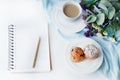 On the white table is a notepad, a pen, a cup of coffee, cupcakes in a plate, a bouquet of flowers Royalty Free Stock Photo