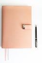 A closed dusty pink notebook lies on a white table, and next to it is a black pen. Royalty Free Stock Photo