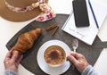A white table with a sweet breakfast. Homemade cappuccino with cinnamon powder and a fresh croissant. Smartphone - old  lifestyle Royalty Free Stock Photo