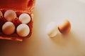 On a white table there is an open orange cardboard package with white chicken eggs, and next to it are two eggs. Healthy nutrition Royalty Free Stock Photo