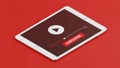A white tablet computer displays a video player interface with a large play button and a prominent red subscribe button on a red Royalty Free Stock Photo