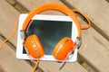 White tablet PC with orange headphones on the wood bench Royalty Free Stock Photo