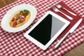 White Tablet PC with Dish, Fork, and Knife on Red Checked Tablecloth Royalty Free Stock Photo