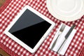 White Tablet PC with Dish, Fork, and Knife on Red Checked Tablecloth Royalty Free Stock Photo