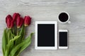 White tablet with a cup of coffee and red flowers lies on a white wooden table