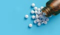 White tablets spilling out of a glass bottle isolated on blue backdrop with space for text