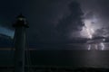 White tall lighthouse on sea shore with blinking light at stormy night for commercial vessels navigation. Thunderstorm