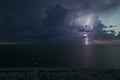 White tall lighthouse on sea shore with blinking light at stormy night for commercial vessels navigation. Thunderstorm