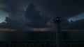 White tall lighthouse on sea shore with blinking light at stormy night for commercial vessels navigation. Thunderstorm