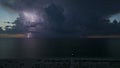 White tall lighthouse on sea shore with blinking light at stormy night for commercial vessels navigation. Thunderstorm