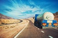 White tanker and trucks driving along picturesque desert mountain highway.