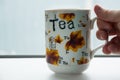 White tea mug with the word tea all over the body, complete with yellow leaves