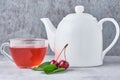 White teapot, herbal tea in glass cup and fresh cherry on a gray background Royalty Free Stock Photo