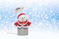 White teddy bear in christmas clothes emerges from open gift box on snowing decorative background