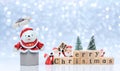 White teddy bear emerges from gift box with Santa Claus dolls are sorting Merry Christmas wooden cubes for on snowing background