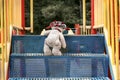 The white teddy bear in the red hat is understood by the blue stairs to the slide on the playground.