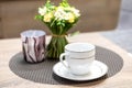 White mug and saucer set. Empty porcelain coffee cup next to decorative flowers and candlestick on wooden table in Royalty Free Stock Photo