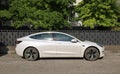 White Tesla Model 3 at the road side in a suburban area. Side view.