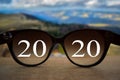 2020 white text with black eye glasses on wooden table over blur autumn landscapes. Business vision happy new year.