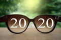 2020 white text with black eye glasses on wooden table over blur autumn landscapes. Business vision happy new year..