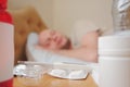 White thermometer on a pack of pills and two bottles with medicine in focus, sick man sleeping in bad out of focus in the Royalty Free Stock Photo